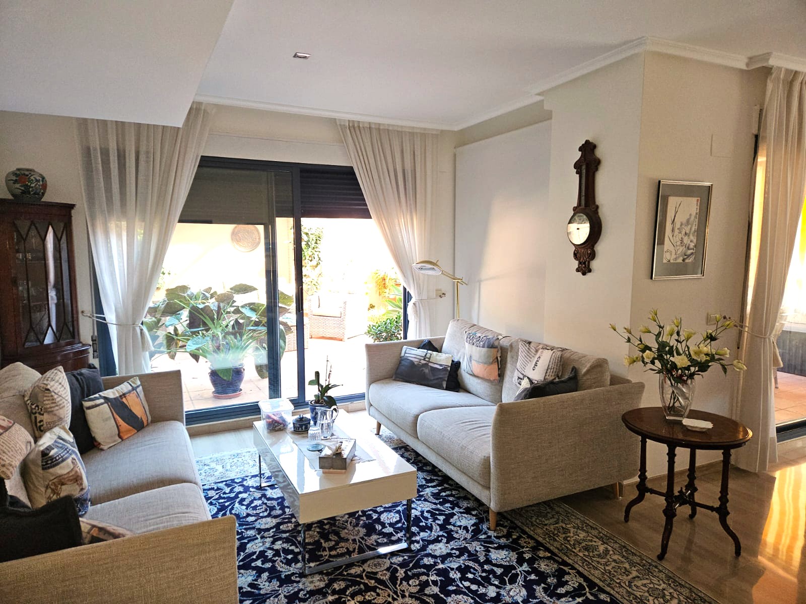 Salón luminoso con dos sofás en tonos neutros, alfombra azul estampada y amplios ventanales correderos con acceso directo a una terraza privada.