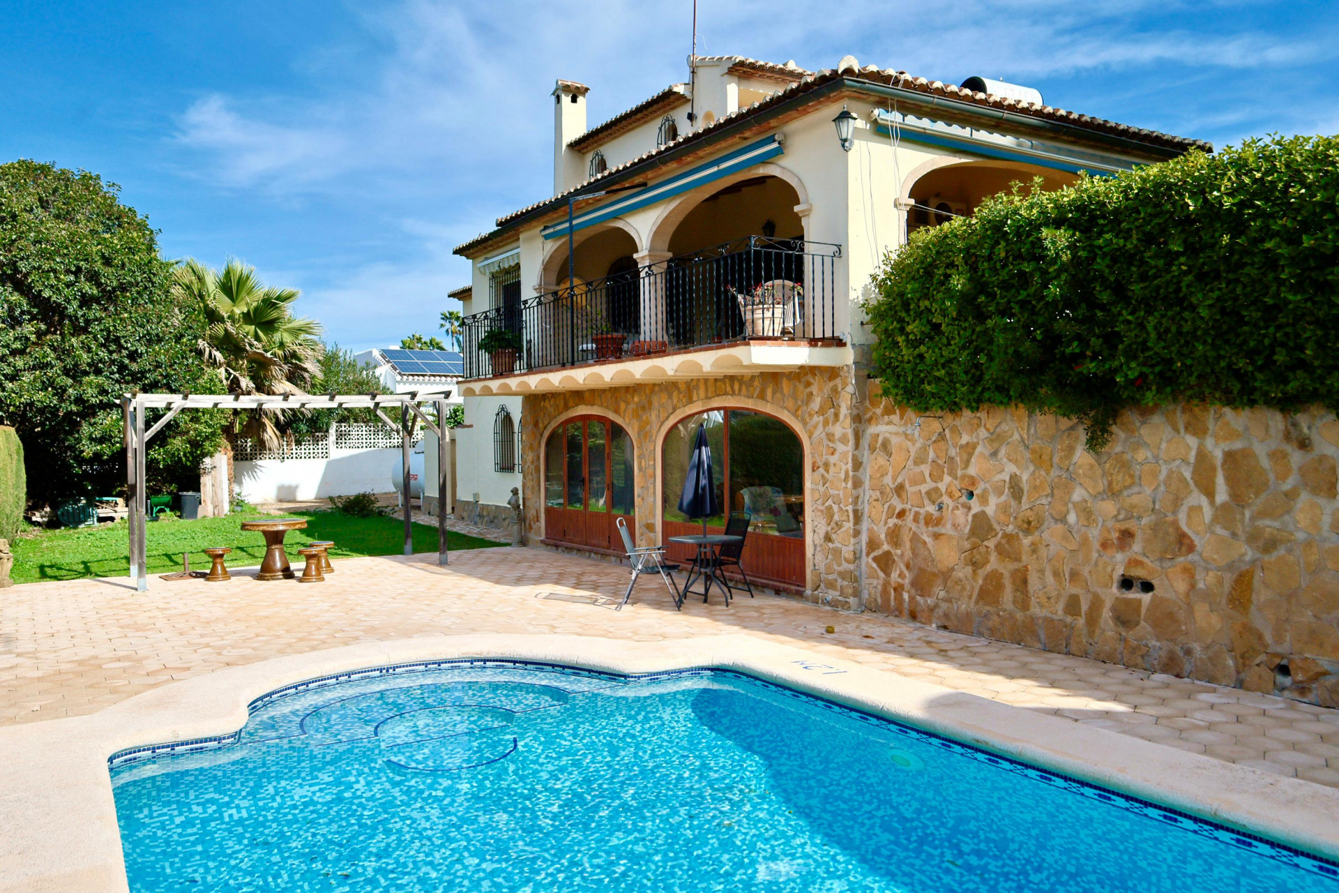 Exterior con piscina privada, fachada de piedra natural, ventanales en arco y amplia terraza superior con arquería tradicional y barandilla de hierro.