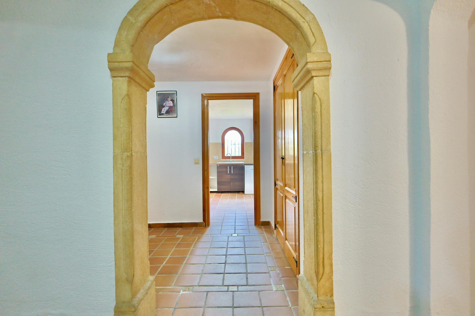 Pasillo de entrada con arco tradicional de piedra Tosca, suelos de baldosa de terracota y armarios empotrados de madera que conducen hacia la cocina.