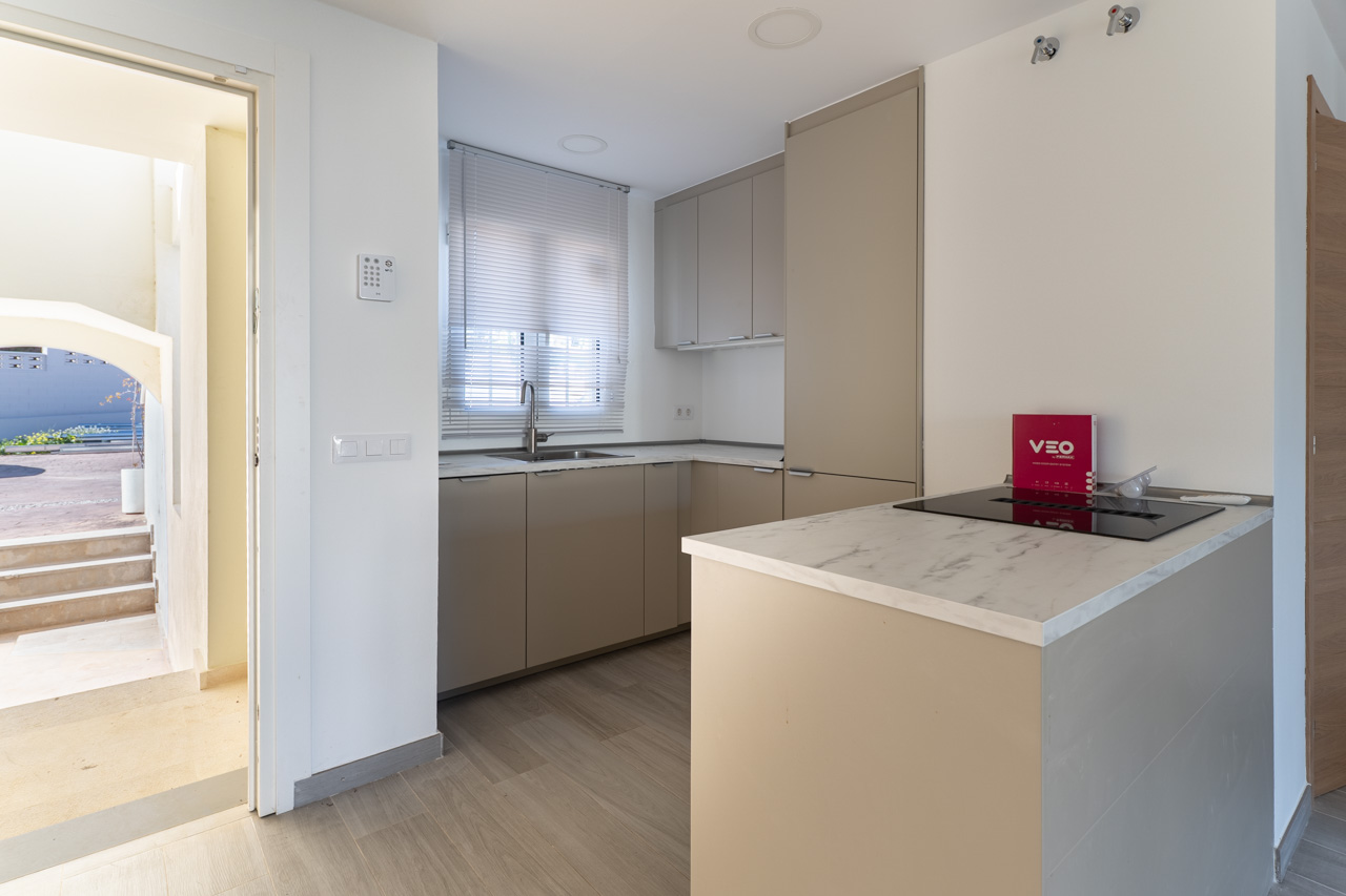 Cocina abierta de diseño funcional con mobiliario en tono topo, encimera de efecto mármol y placa de inducción, integrada en un espacio luminoso con suelo de madera clara.