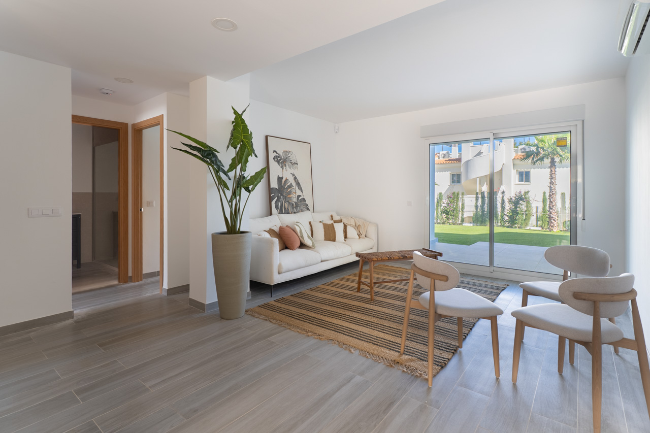 Salón luminoso con suelos de gres cerámico imitación madera, mobiliario de tonos neutros y acceso directo al jardín privado a través de un gran ventanal corredero.