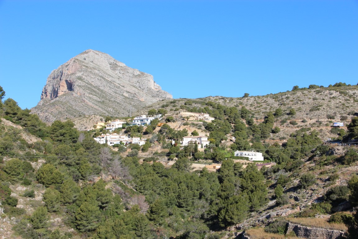 Vista panorámica de la ladera de La Corona en Jávea, con vegetación mediterránea y villas blancas bajo el imponente macizo del Montgó.