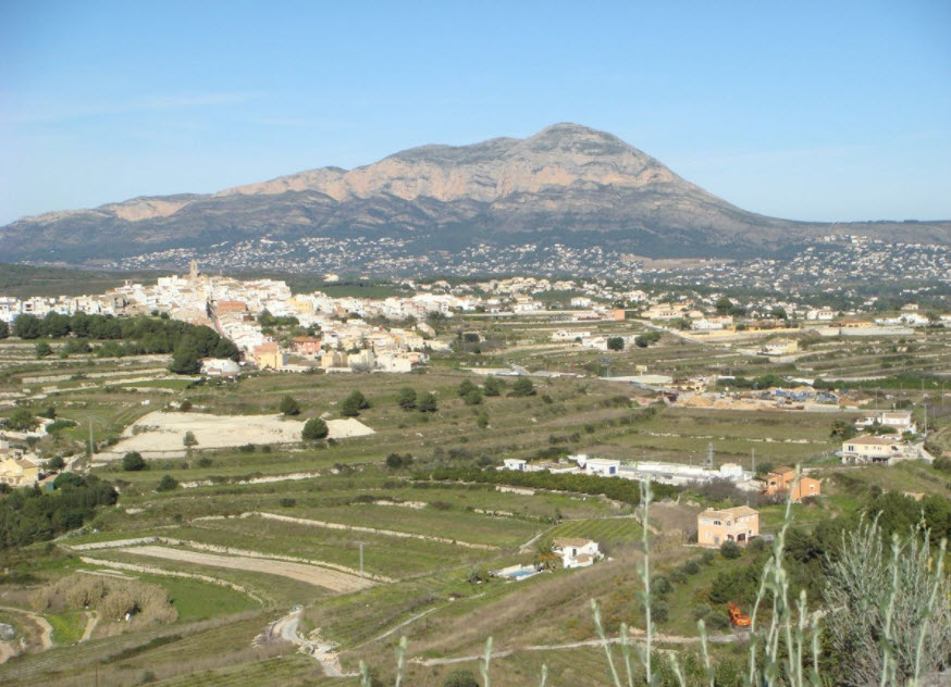 Vista panorámica del terreno abancalado en Benitachell, con el macizo del Montgó al fondo y el núcleo urbano integrado en el paisaje mediterráneo.