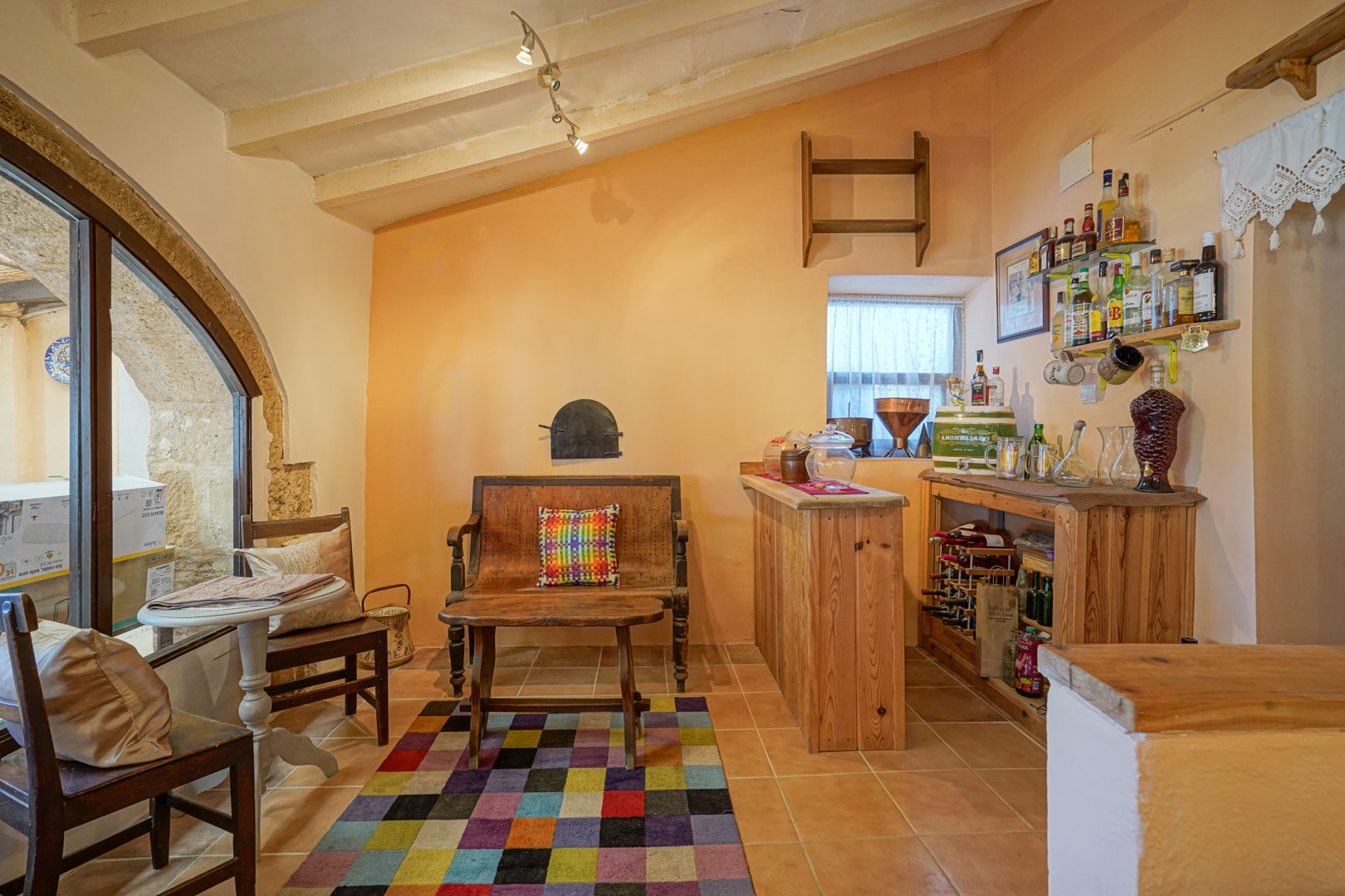 Rincón de bar tradicional con barra de madera, vigas vistas en el techo inclinado y un arco de piedra tosca original que aporta carácter rústico.